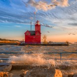 Article thumbnail: Holland, MI, USA-Ocober 12, 2019: The sun sets over the Big Red Lighthouse on Lake Michigan as waves crash the shore in Holland, Michigan.