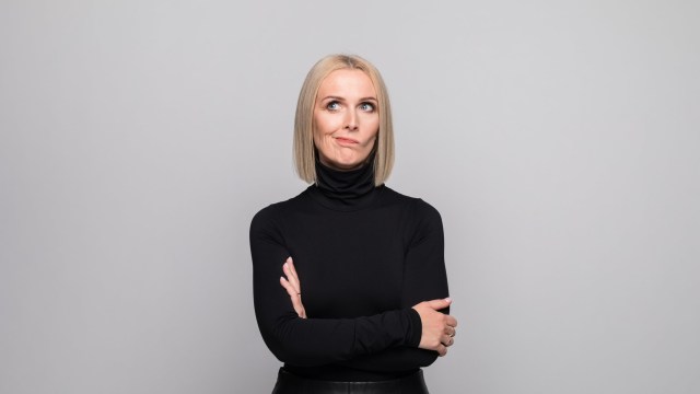 Article thumbnail: Portrait of beautiful mature woman wearing black turtleneck, standing with arms crossed and looking away. Studio shot, grey background.