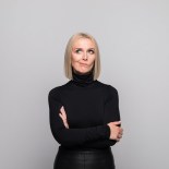 Article thumbnail: Portrait of beautiful mature woman wearing black turtleneck, standing with arms crossed and looking away. Studio shot, grey background.