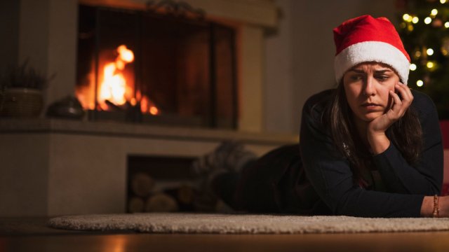 Article thumbnail: Young woman laying on carpet alone at home around fireplace and Christmas decoration on background.