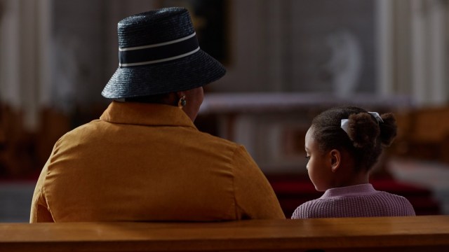 Rear view of African American grandmother sitting on bench with little girl during ministration in church